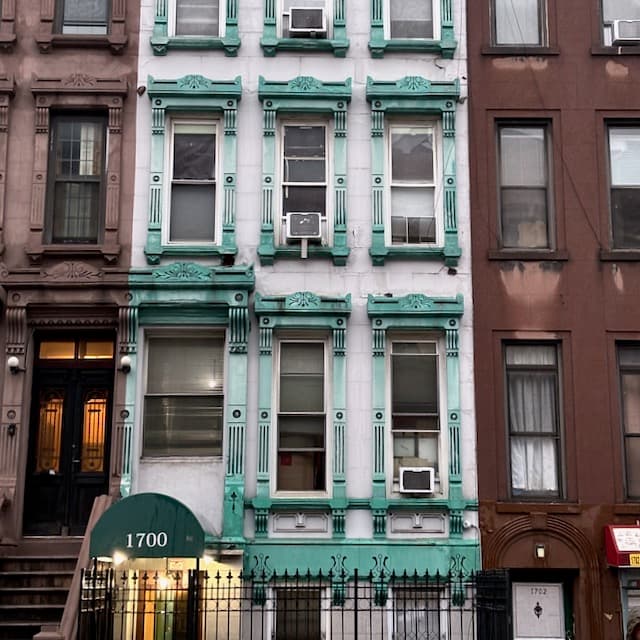 Brownstone row with striking mint-green facade, ornate windows, numbered 1700, between darker buildings.