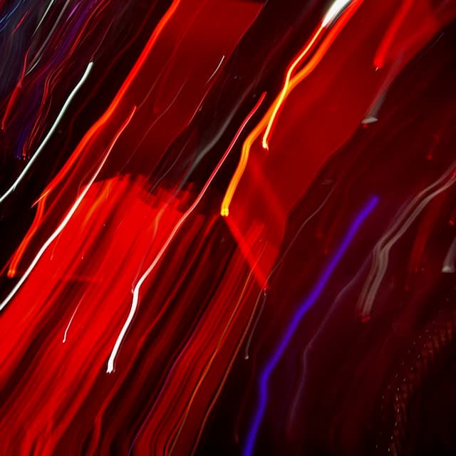 Abstract image of blurred red, orange, and purple light streaks, suggesting fast motion or long exposure.