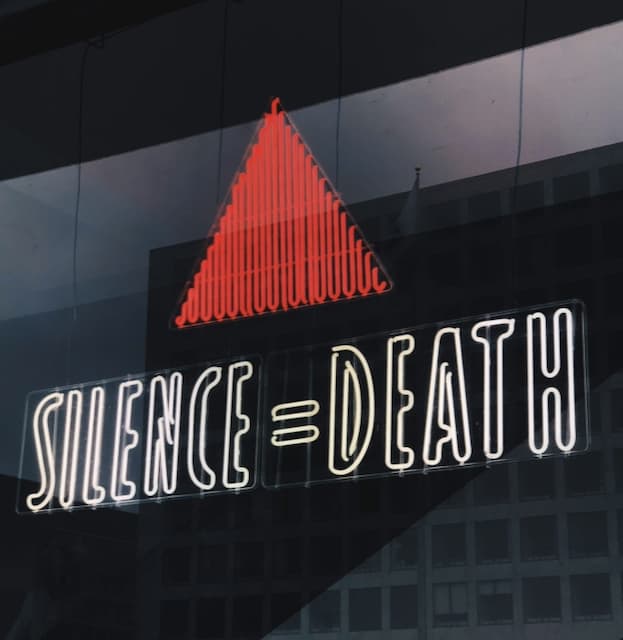 Illuminated neon sign of a red triangle above the words, 'SILENCE = DEATH'