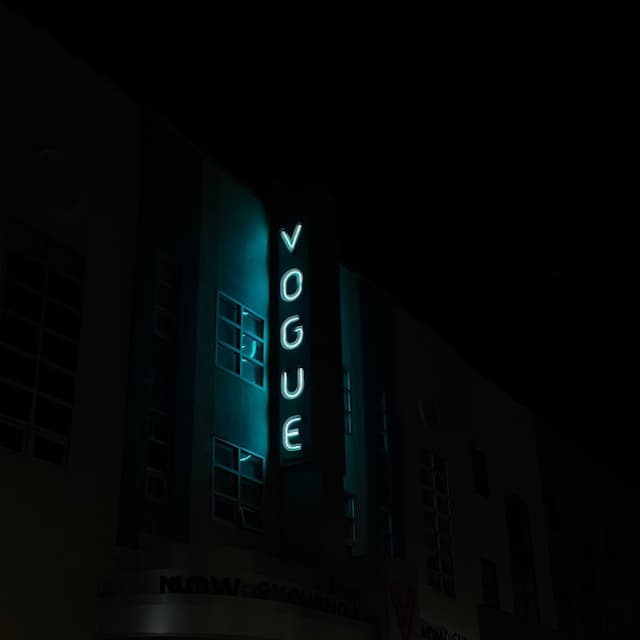 A neon blue sign emitting light against a building that reads, VOGUE