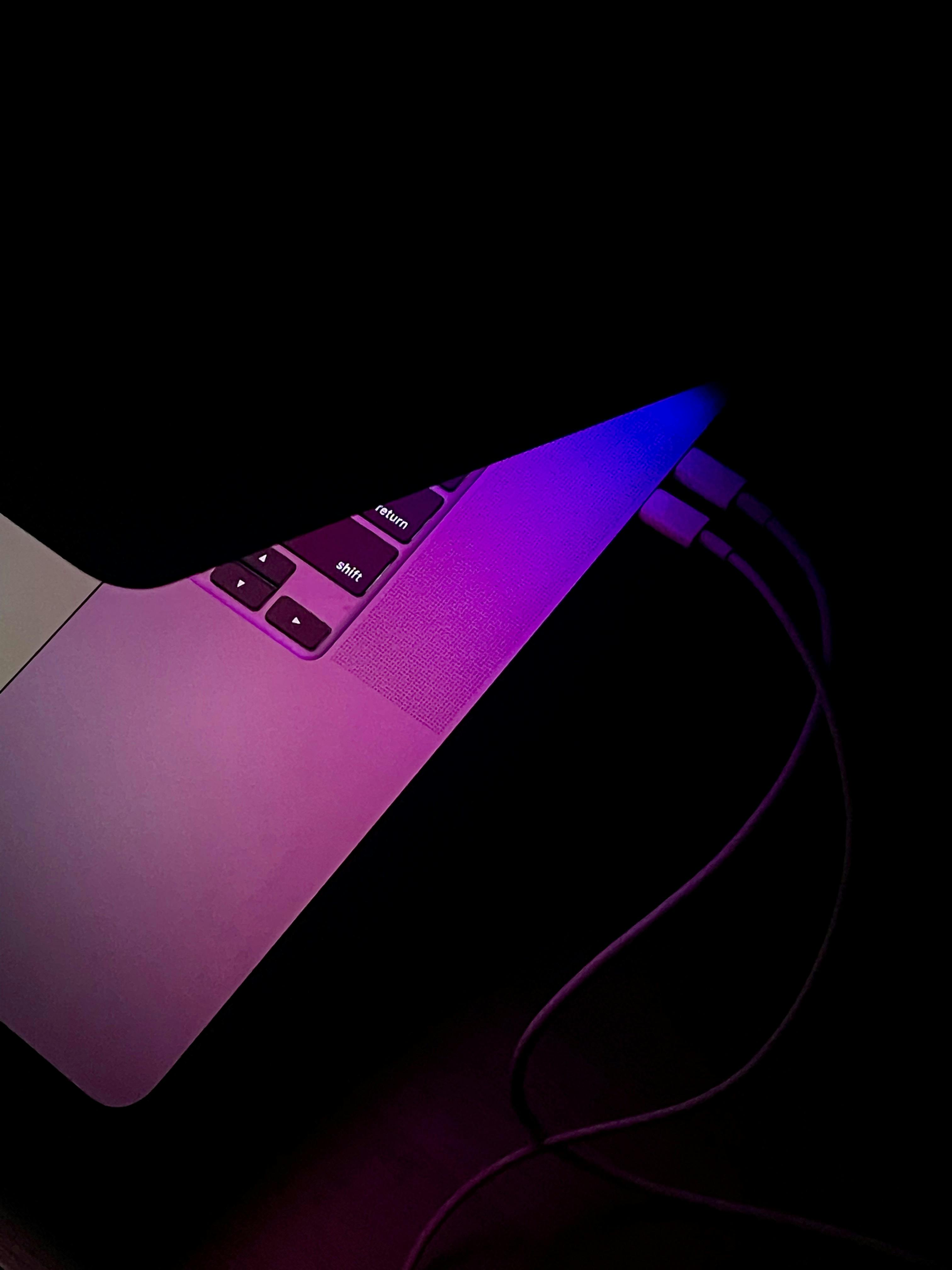 A half-open MacBook Pro in the dark, emitting blue and purple light from the screen