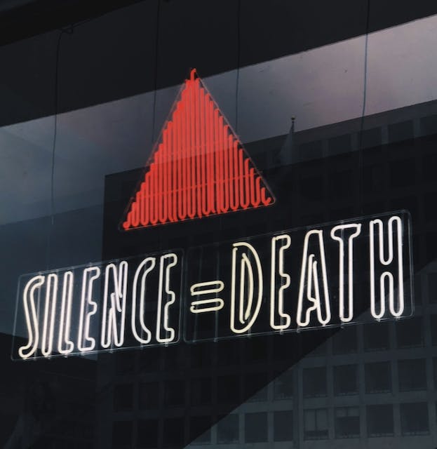 Illuminated neon sign of a red triangle above the words, 'SILENCE = DEATH'