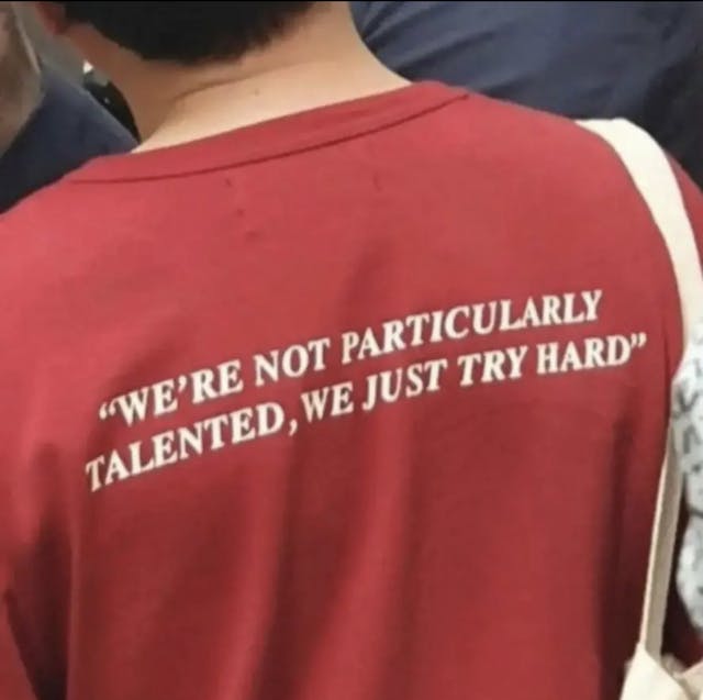 Back of red t-shirt that reads, 'WE'RE NOT PARTICULARLY TALENTED, WE JUST TRY HARD'