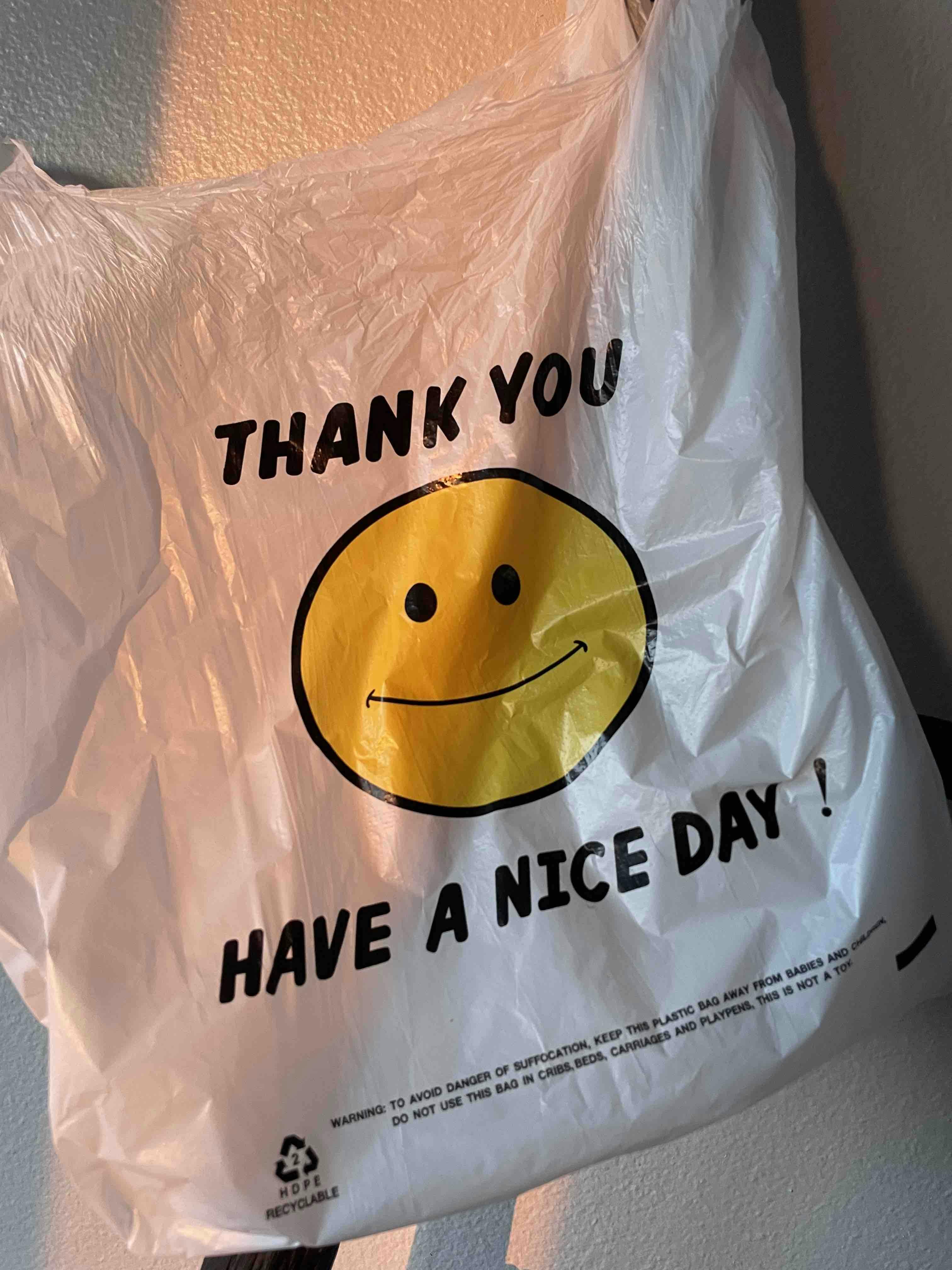 Plastic takeout bag with a big yellow snmiley face and the words, thank you have a nice day