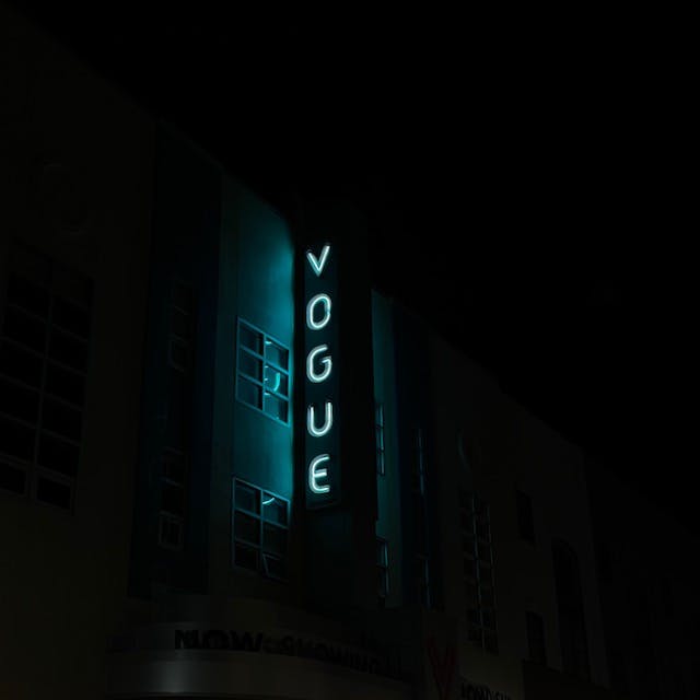 A neon blue sign emitting light against a building that reads, VOGUE